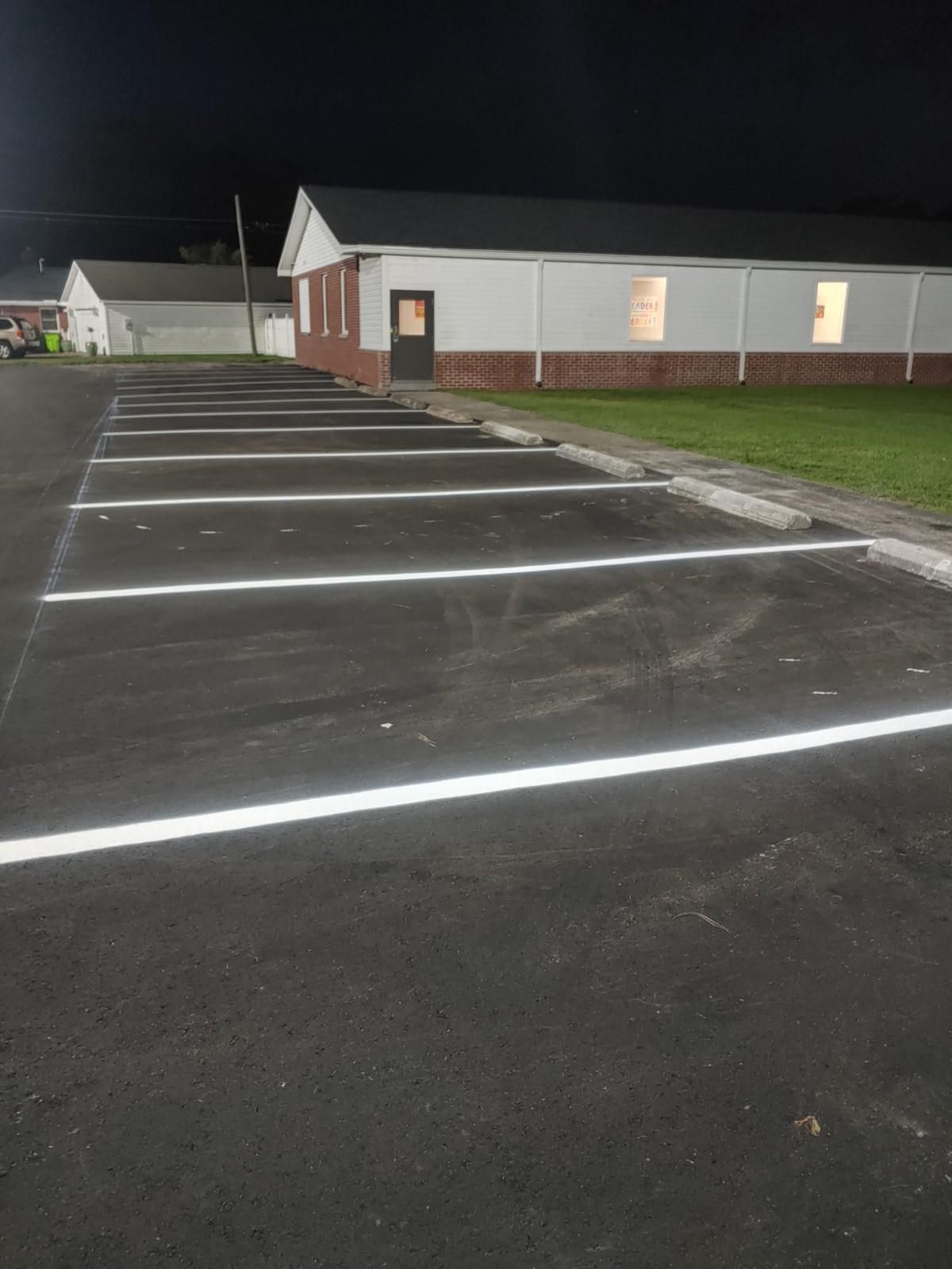 Newly paved parking spaces with white painted lines in front of a brick building.