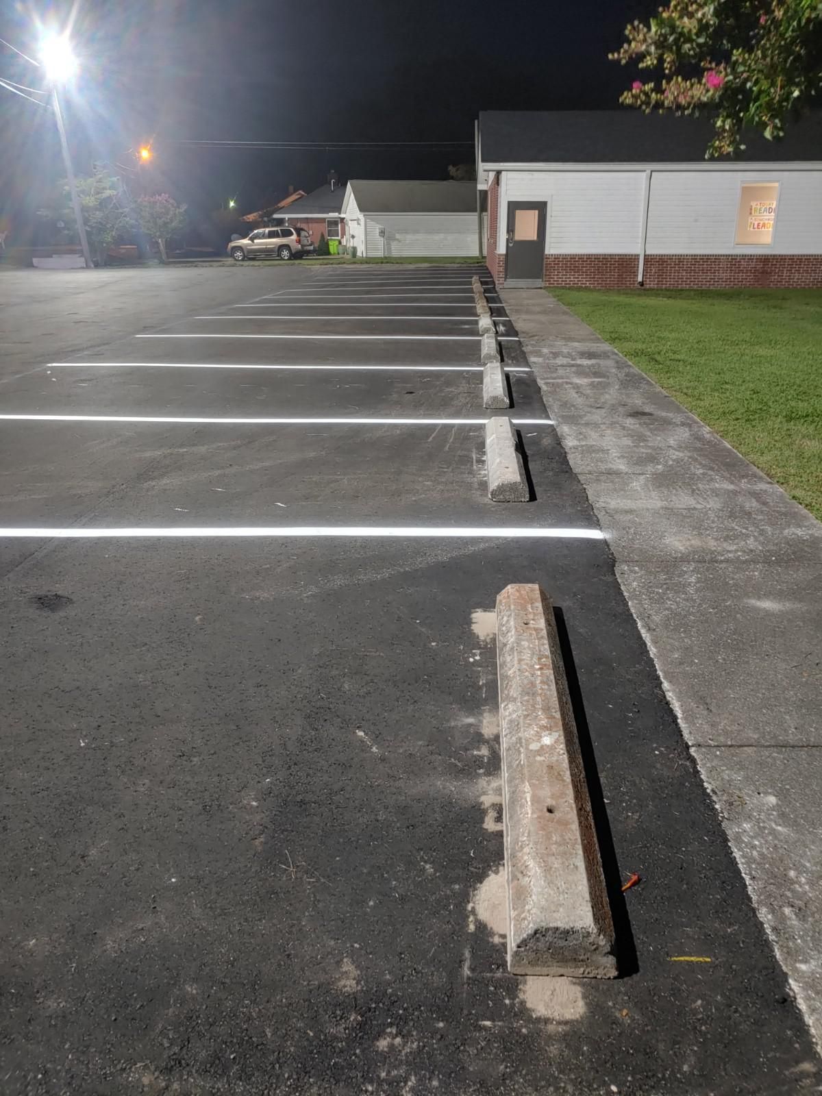 Asphalt parking lot at night with white lines, concrete bumpers, and a building on the right.