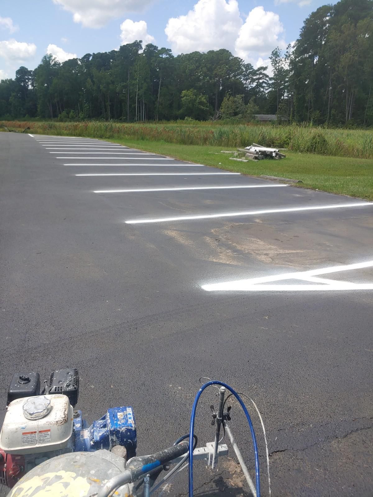 Asphalt surface with white lines, likely a parking area being marked. Striping machine visible.