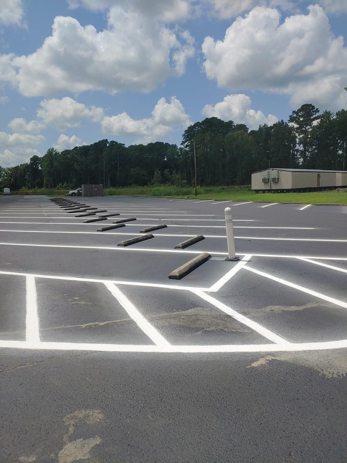 Empty asphalt parking lot with white painted lines and wheel stops, with a cloudy sky backdrop.