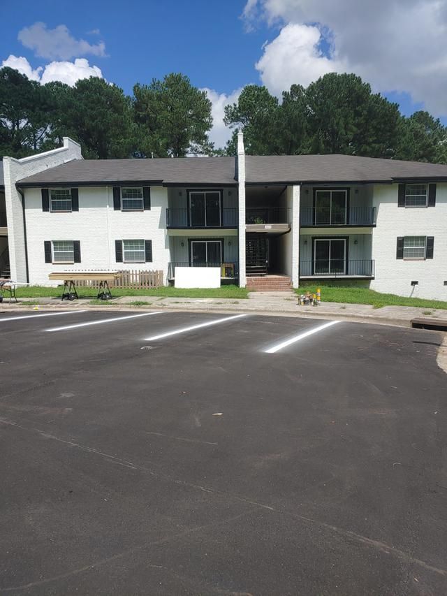 White apartment building with black trim, parking lot, and trees in the background.