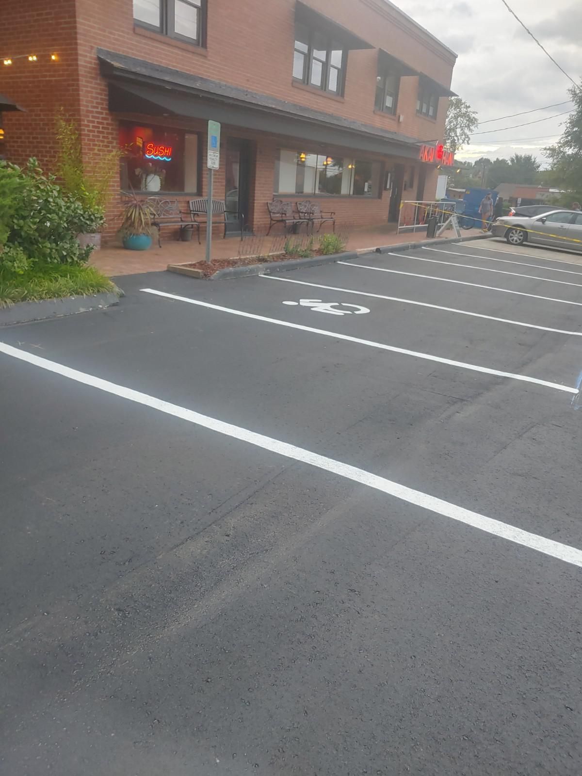 Exterior of a brick building with a newly paved parking lot, including a designated accessible parking space.