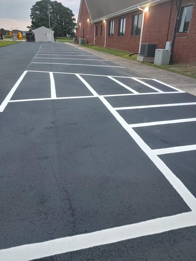 Newly painted black asphalt parking lot with white parking space lines. Brick building in background.