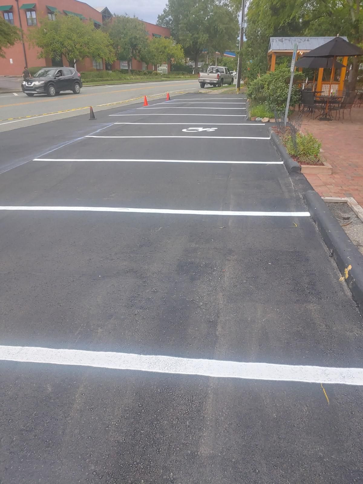 Asphalt parking spaces with white lines, orange cones, and parked vehicles. Trees and a building are in the background.