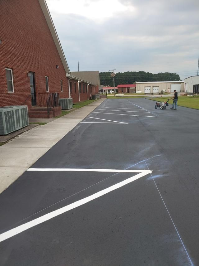 Asphalt parking lot with white painted markings; a person painting lines. Brick building on the left.