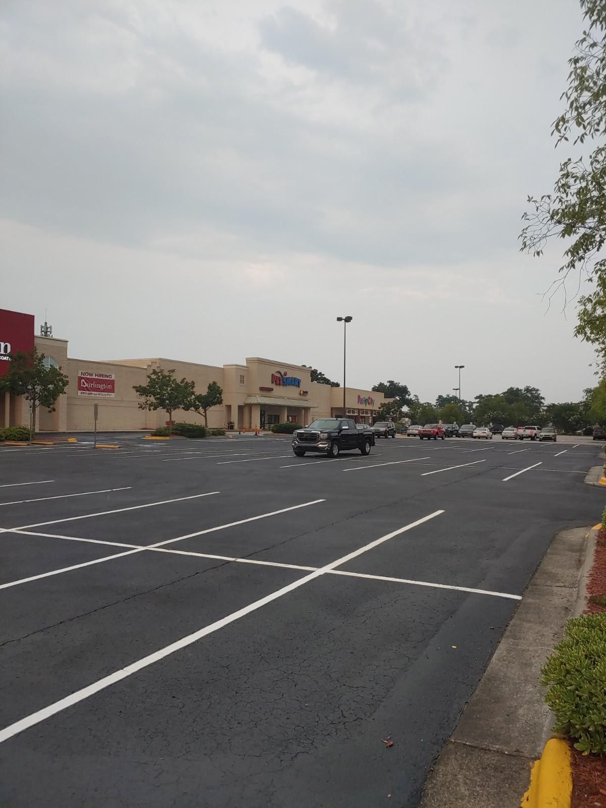 Empty parking lot in front of a beige-colored shopping center under a cloudy sky.