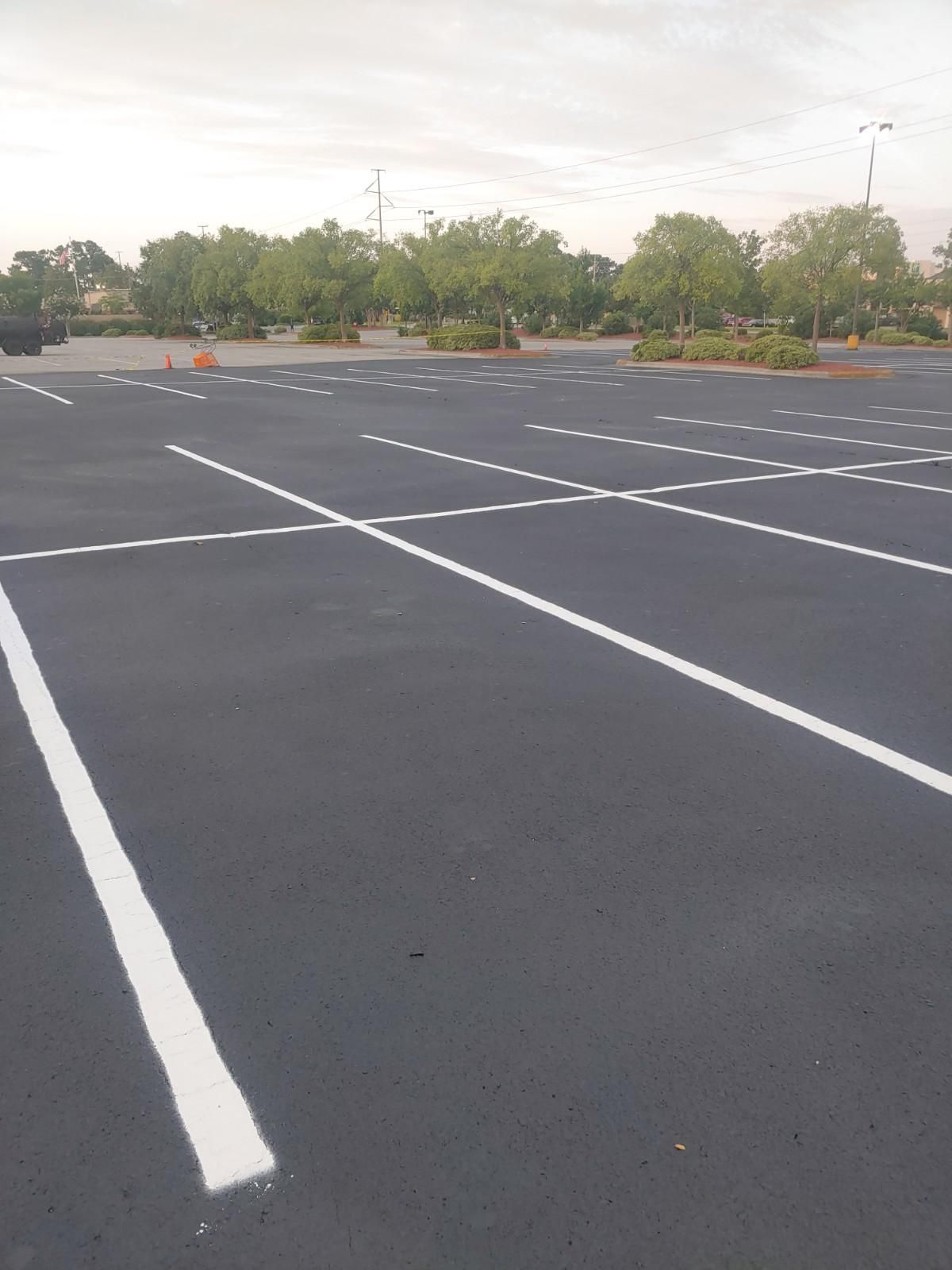 Empty parking lot with white painted lines. Trees and a cloudy sky in the background.