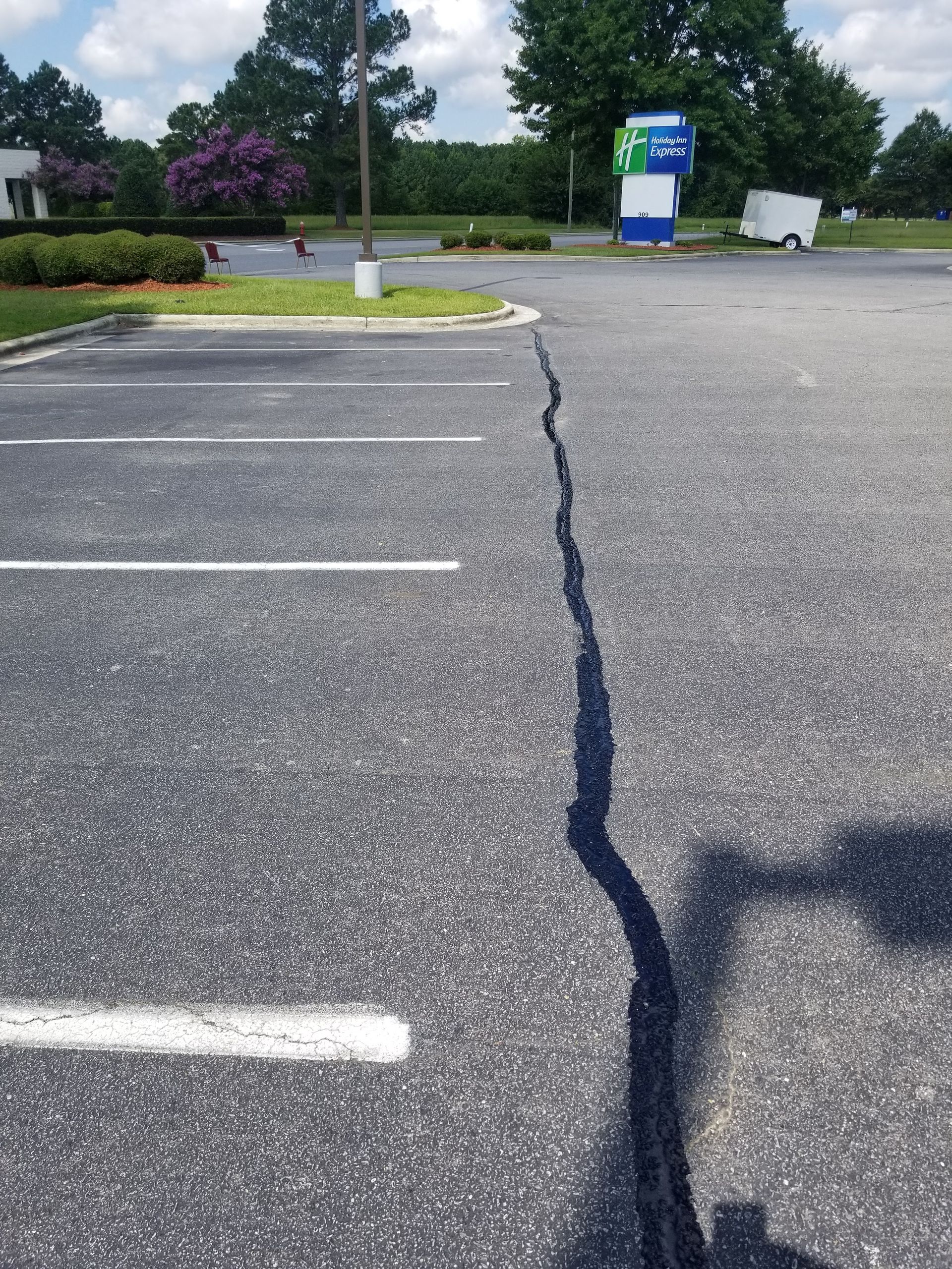 Asphalt parking lot with a long, filled crack; white parking lines, portable toilets visible.