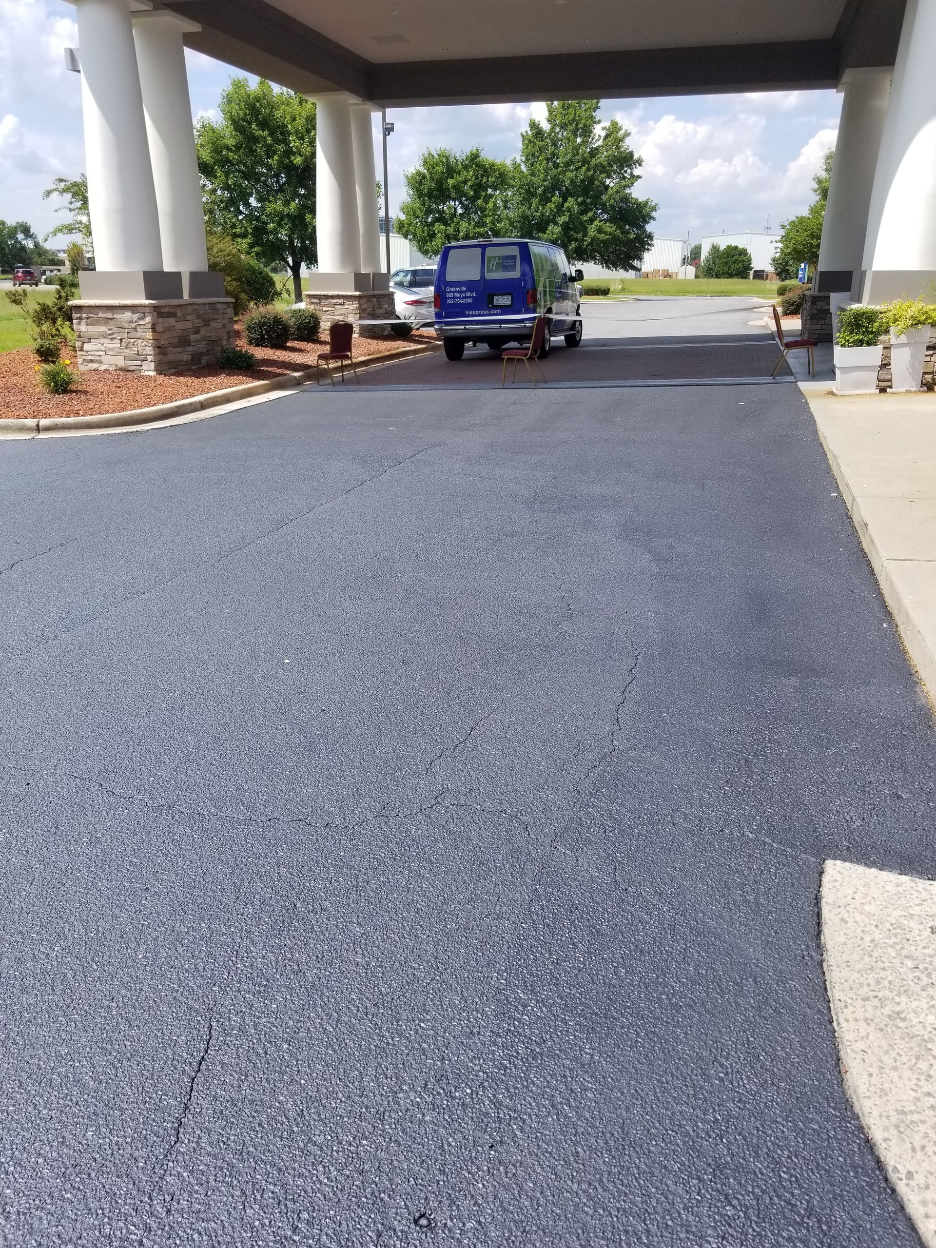 Asphalt driveway under a hotel awning, leading to a blue van parked in the distance.