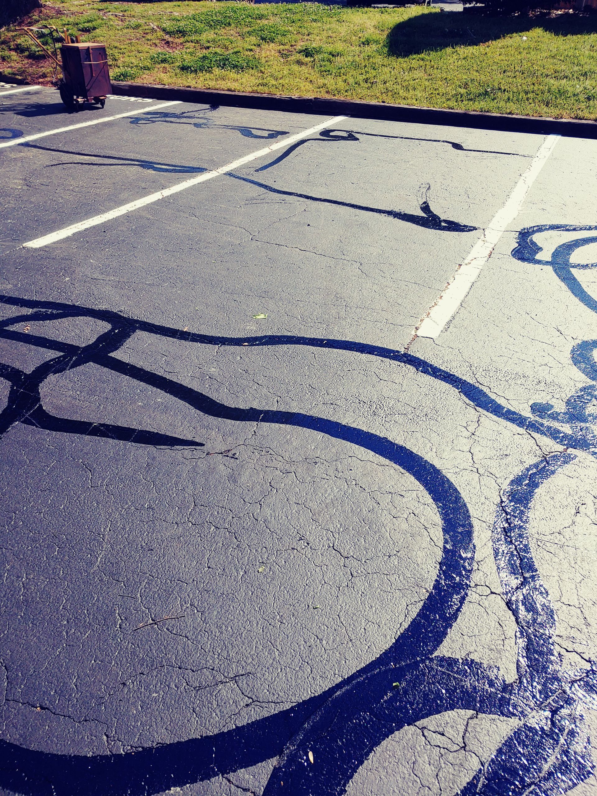 Asphalt parking lot with faded lines and dark tire tracks; brick post and grass visible in background.
