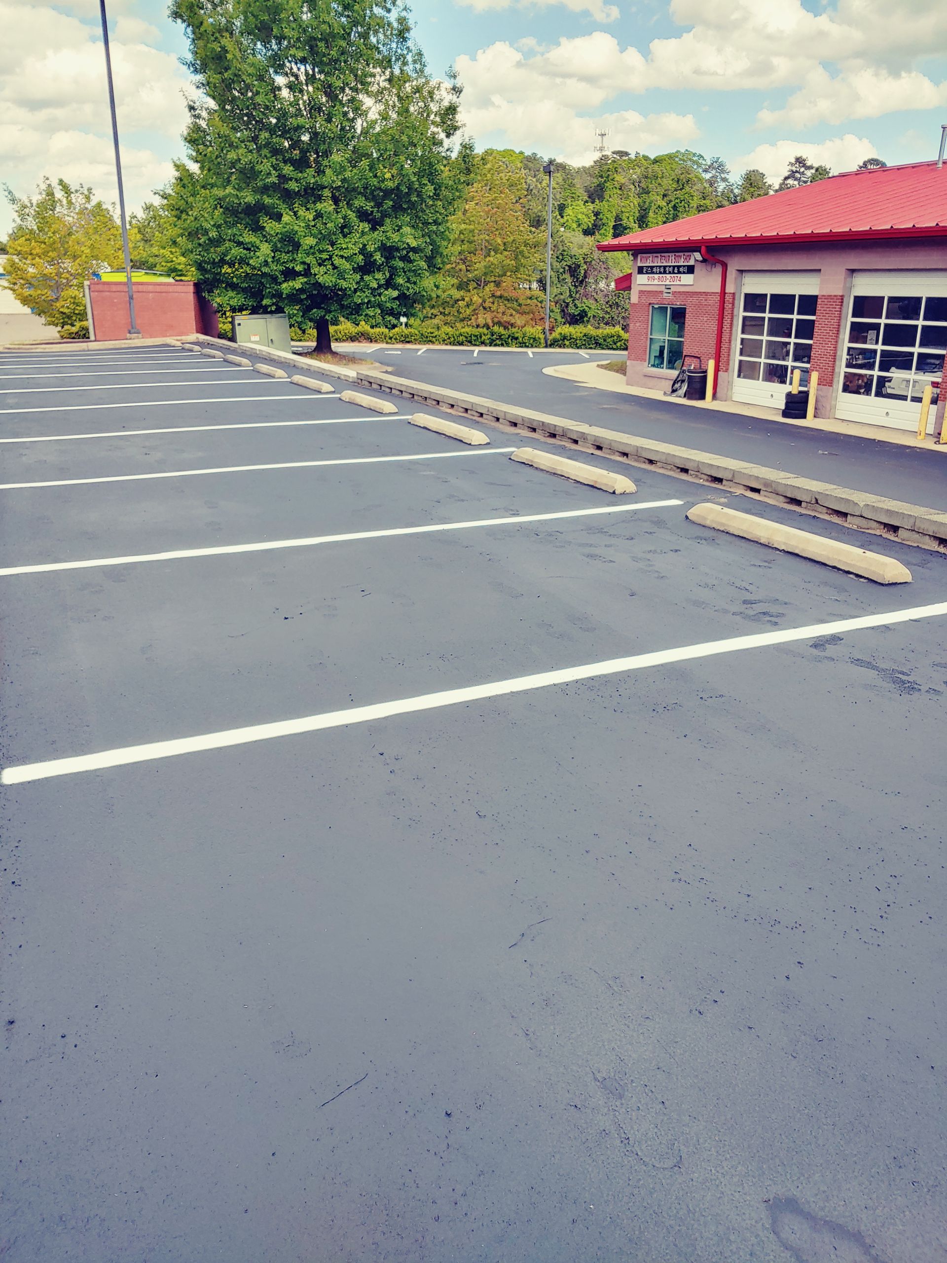 Empty asphalt parking lot with white lines and wheel stops, near a brick building.