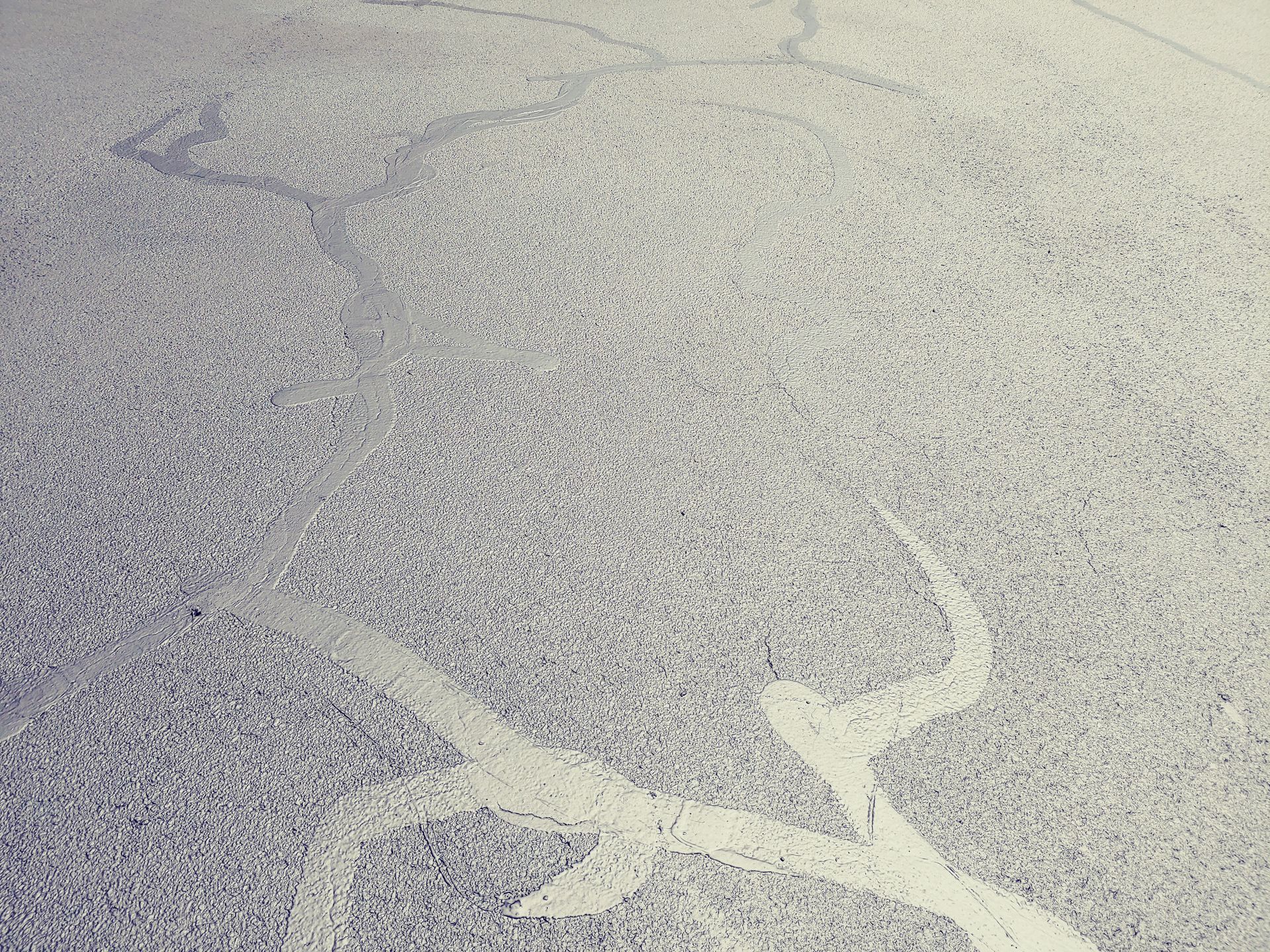 Gray textured pavement with pale white curving lines.