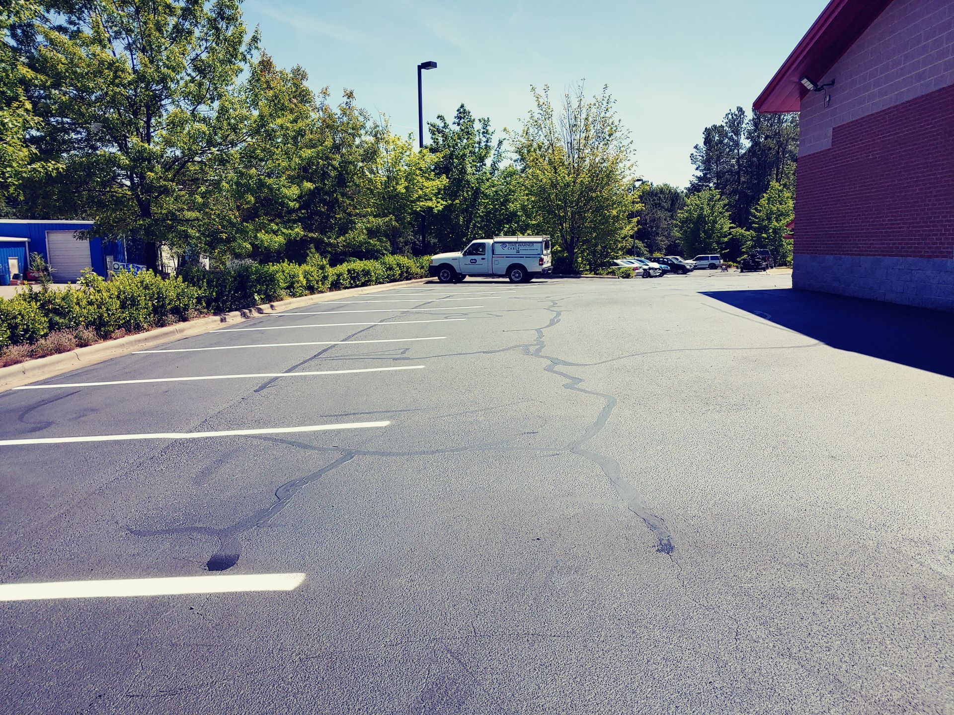 Asphalt parking lot with cracked surface and white painted lines; a white truck is parked further back.