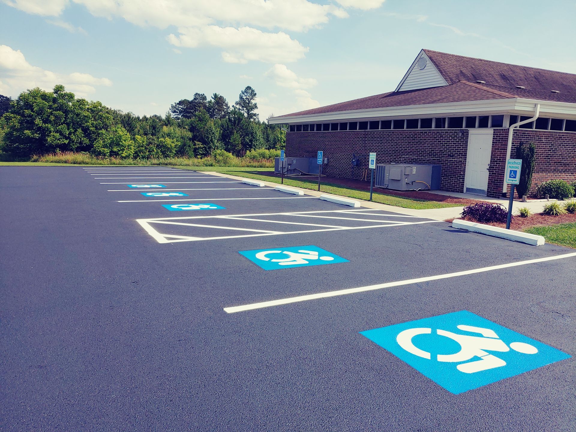 Asphalt parking lot with blue wheelchair-accessible symbols. A building is in the background.
