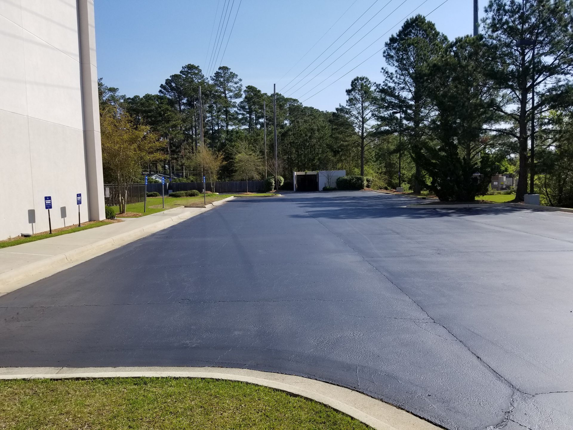 Black asphalt parking lot next to a building and grass, with trees in the background.