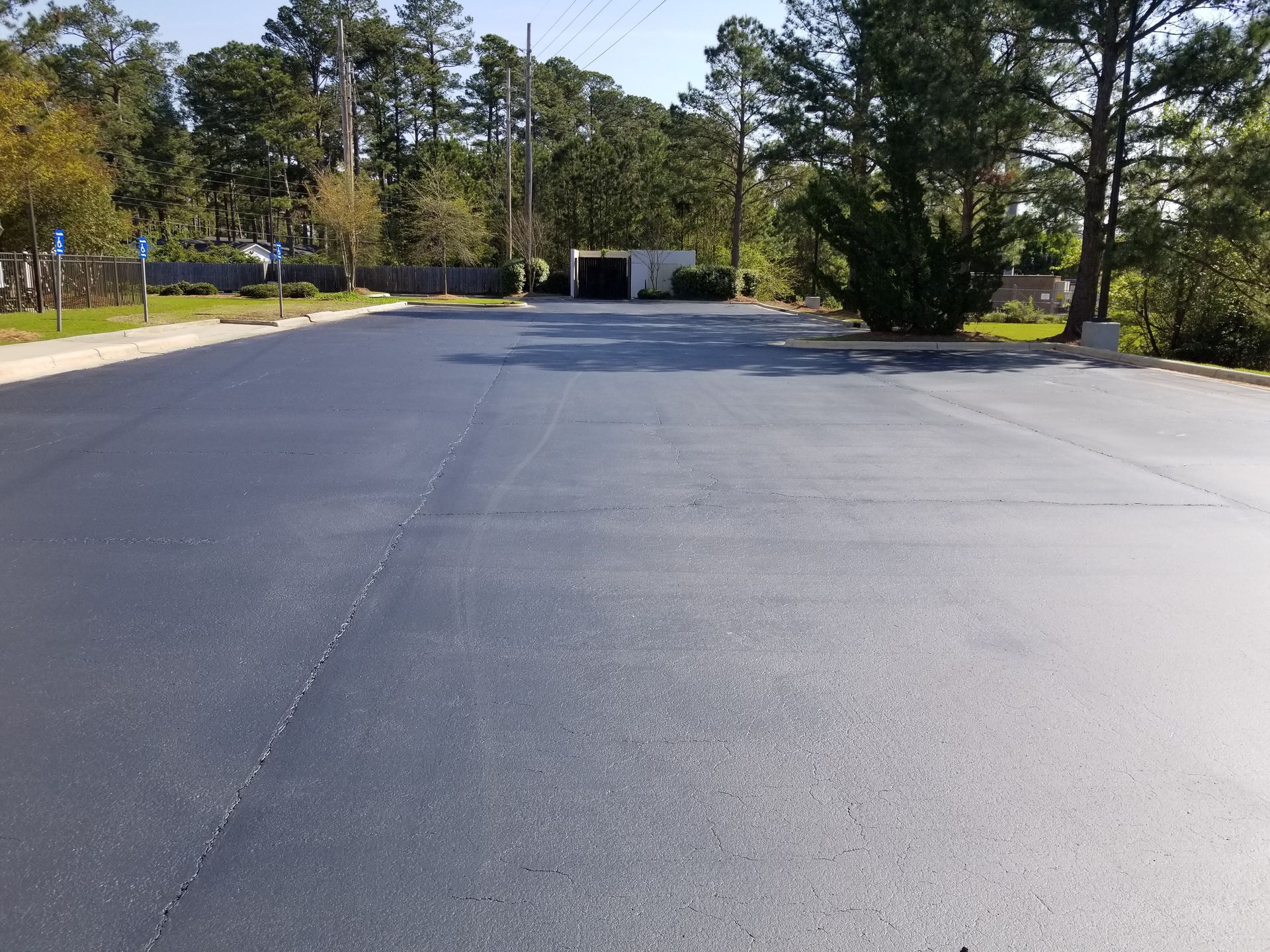 Newly paved asphalt parking lot on a sunny day with trees in the background.