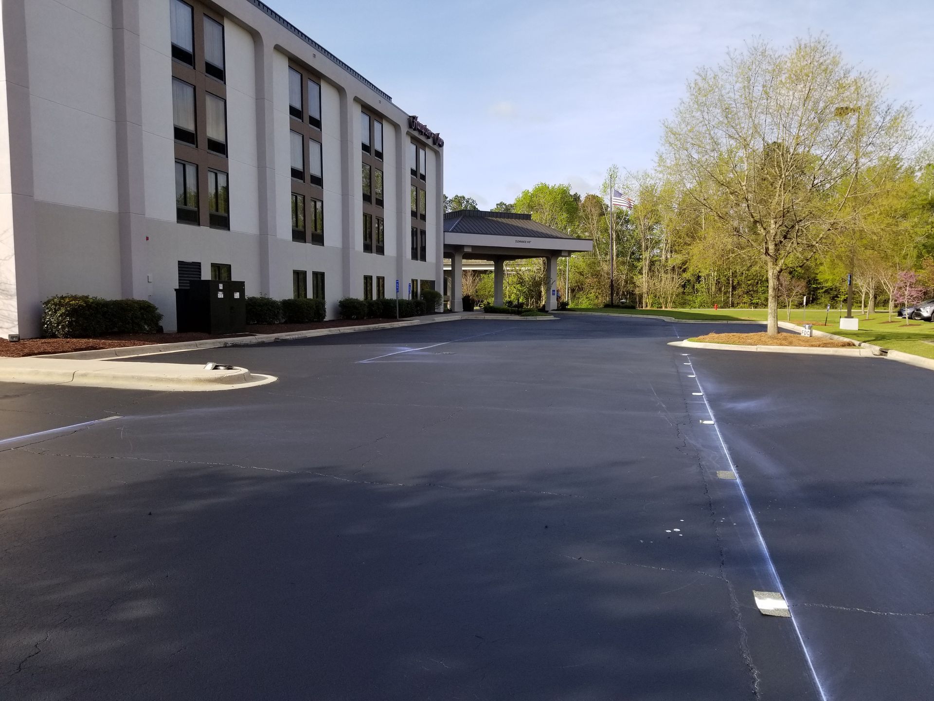 Hotel exterior with asphalt parking lot and small trees on a sunny day.