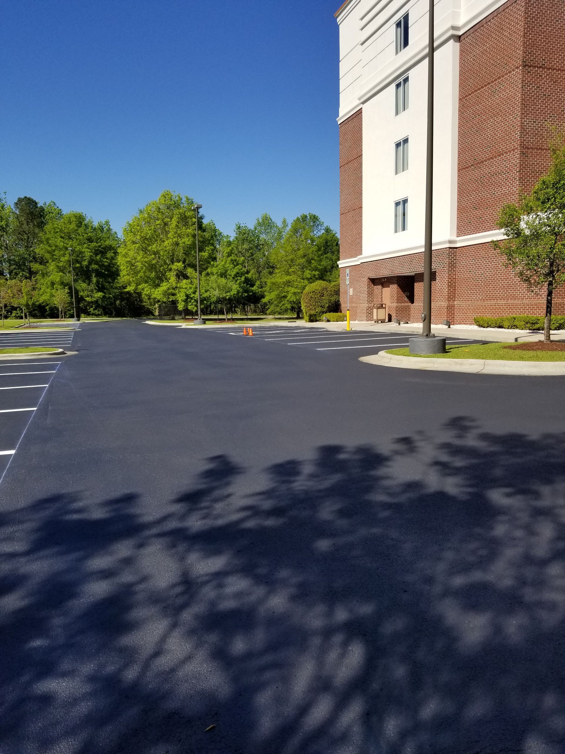 Newly paved asphalt parking lot next to a brick building on a sunny day.