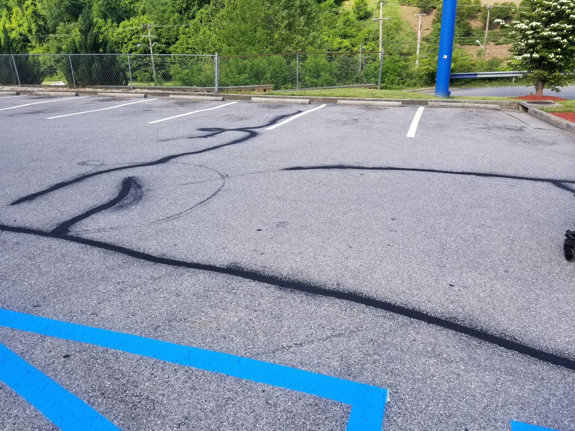 Asphalt parking lot with blue handicap space lines and dark cracks filled in.
