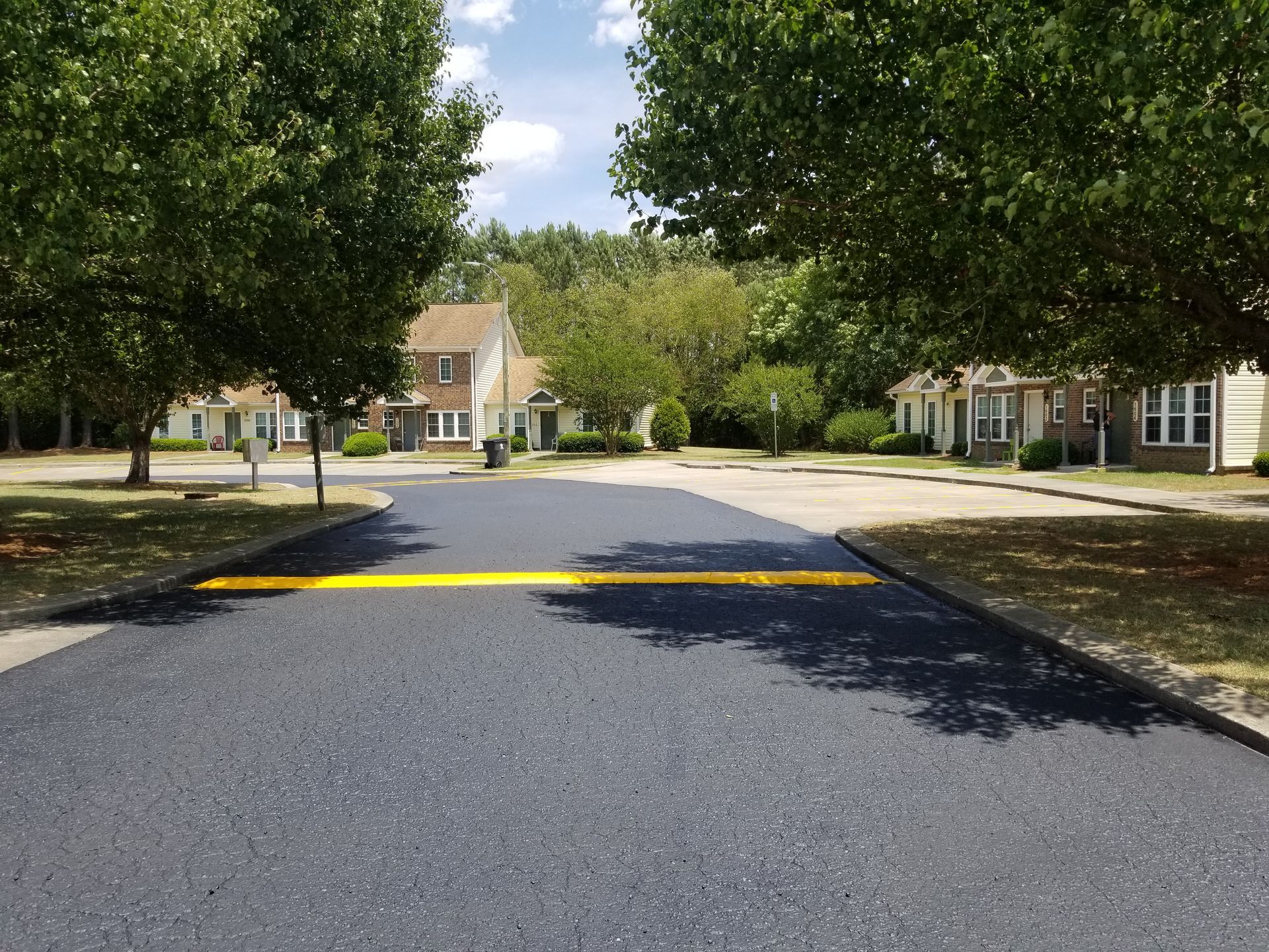 Paved road with speed bump leading to houses under green trees on a sunny day.