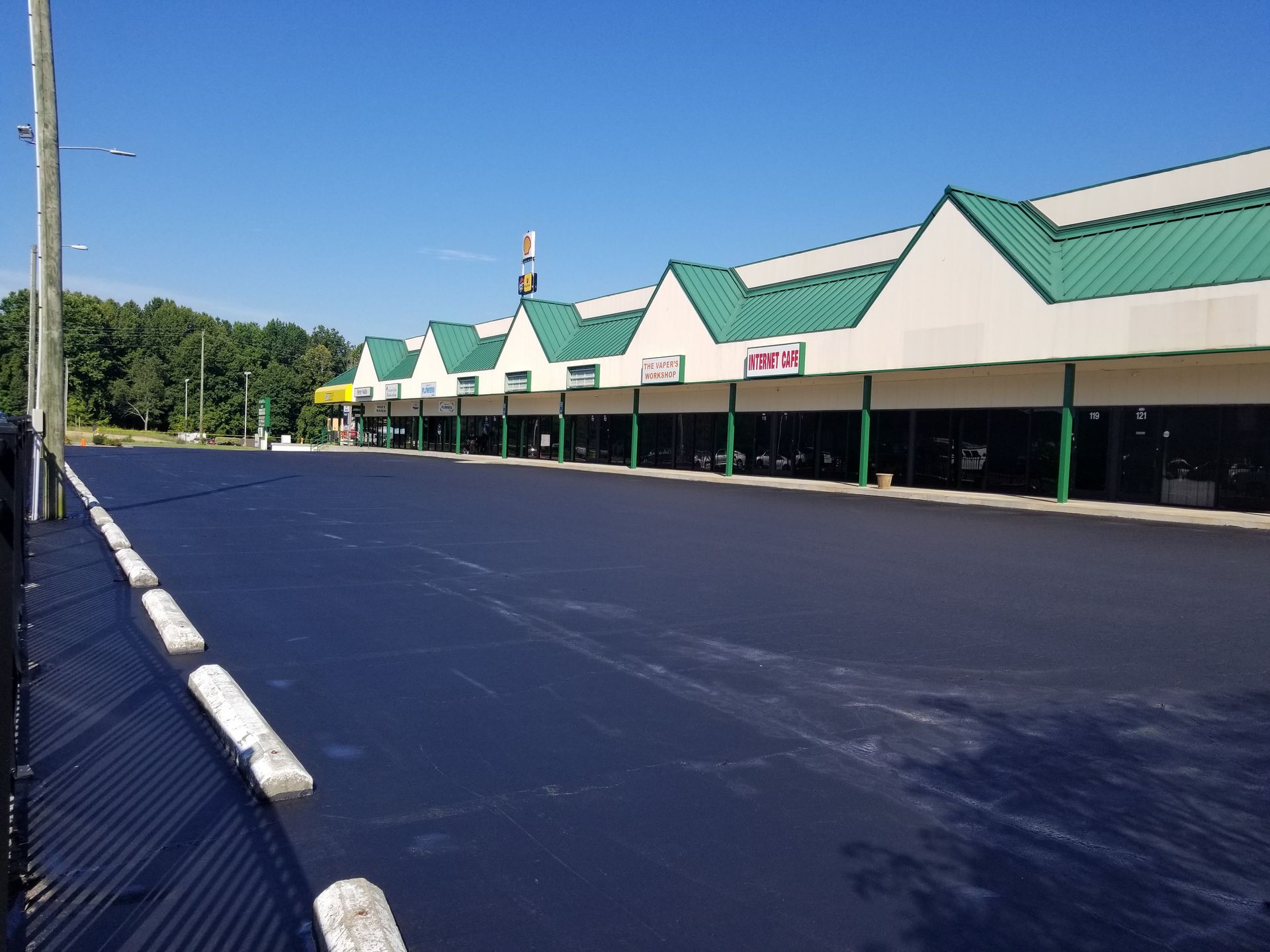 Empty strip mall with black asphalt parking lot on a sunny day. Green roof, white trim.