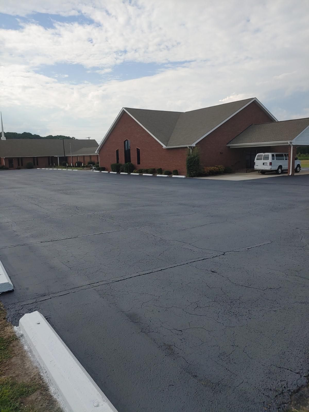 Church building with red brick exterior and a large parking lot on a cloudy day.