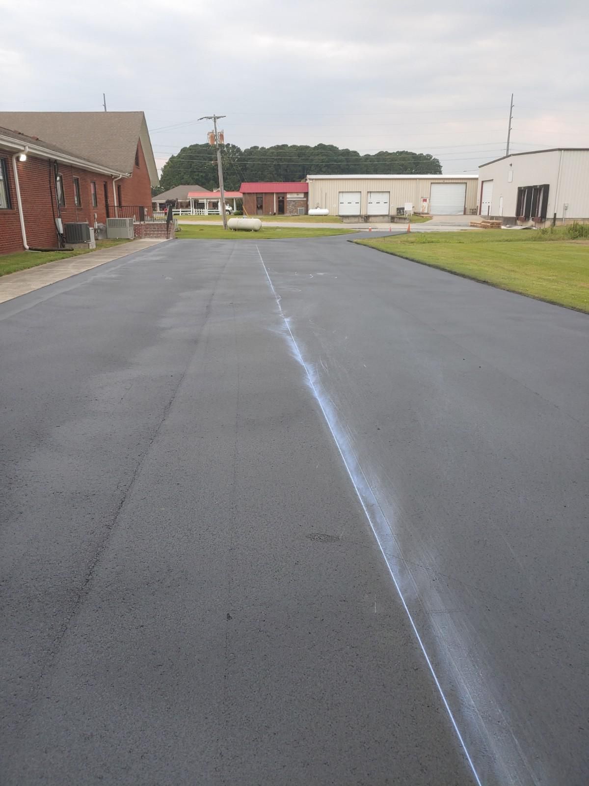 Newly paved asphalt road with a white chalk line, buildings in the background.