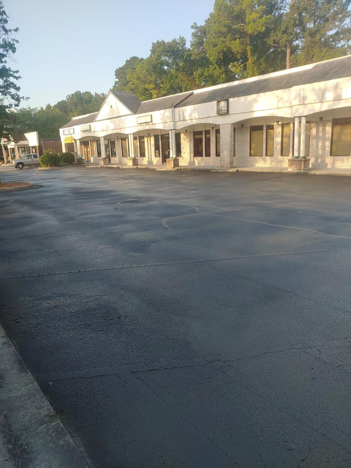 Exterior of a commercial strip mall with a freshly paved asphalt parking lot.