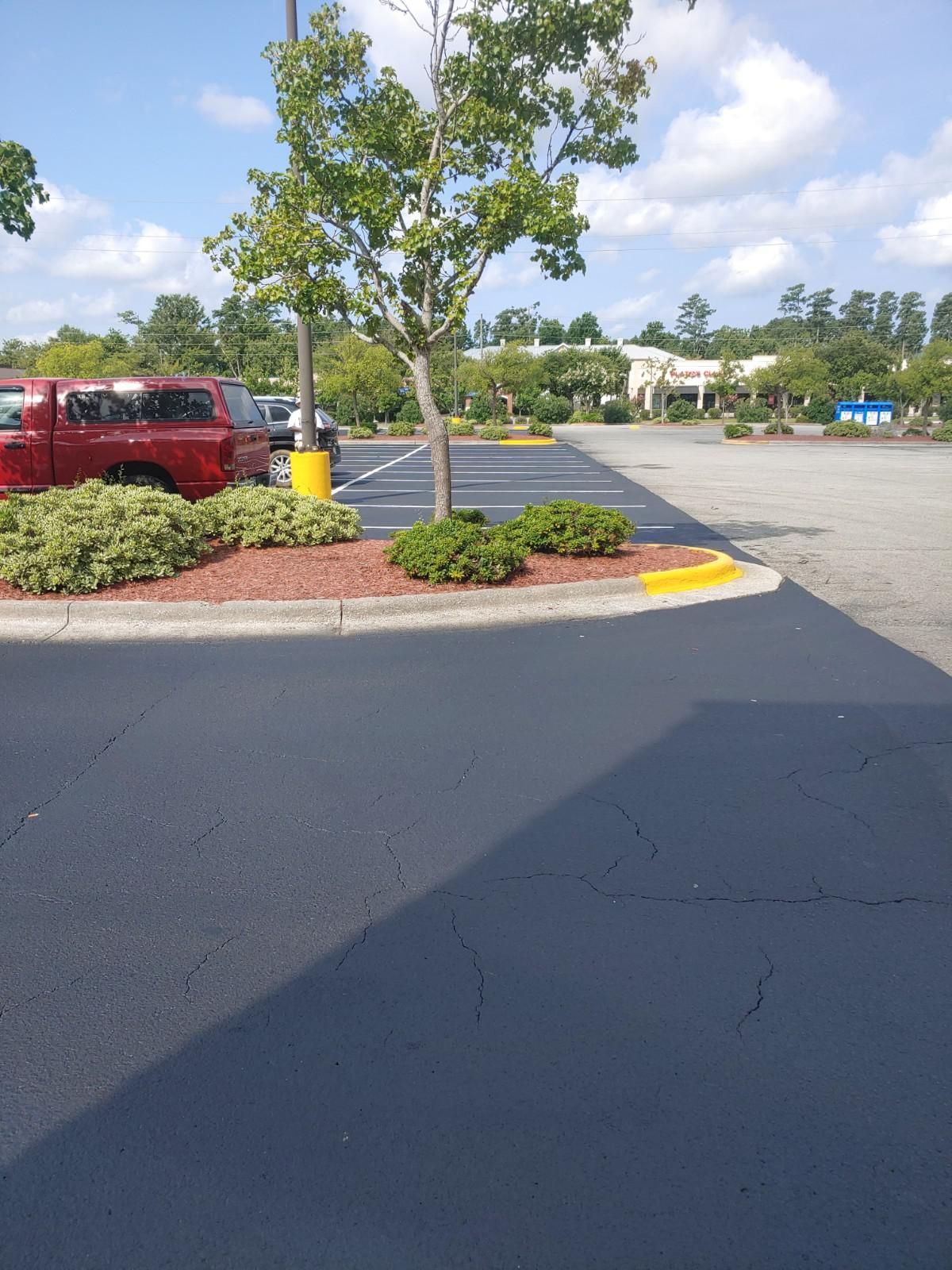 Parking lot with newly paved dark surface, small trees, and red truck.
