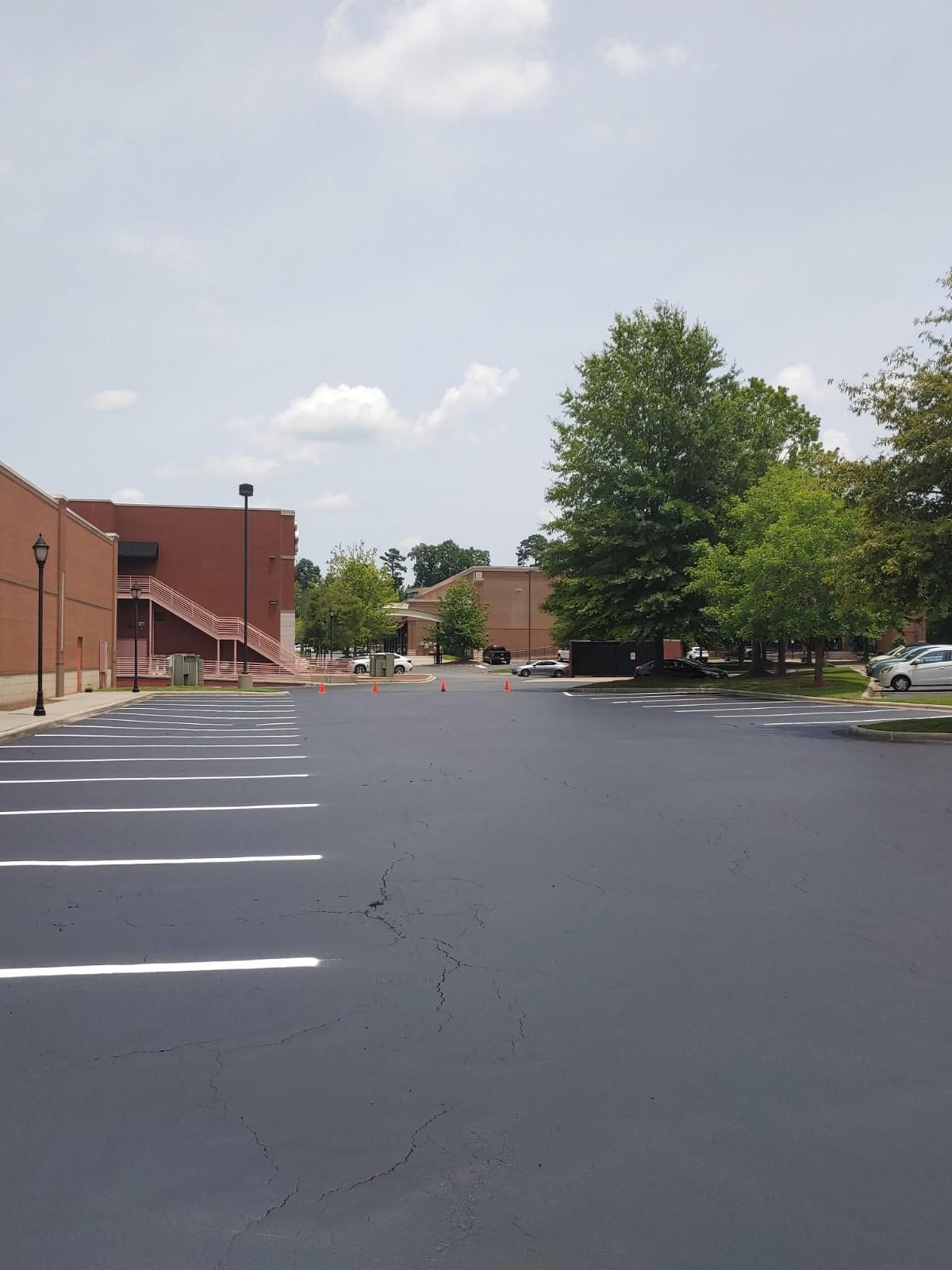 Empty asphalt parking lot next to a brick building and trees on a sunny day.