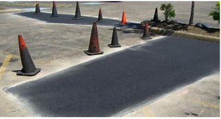 Asphalt repair with traffic cones in a parking lot. Newly laid black asphalt contrasts with existing pavement.