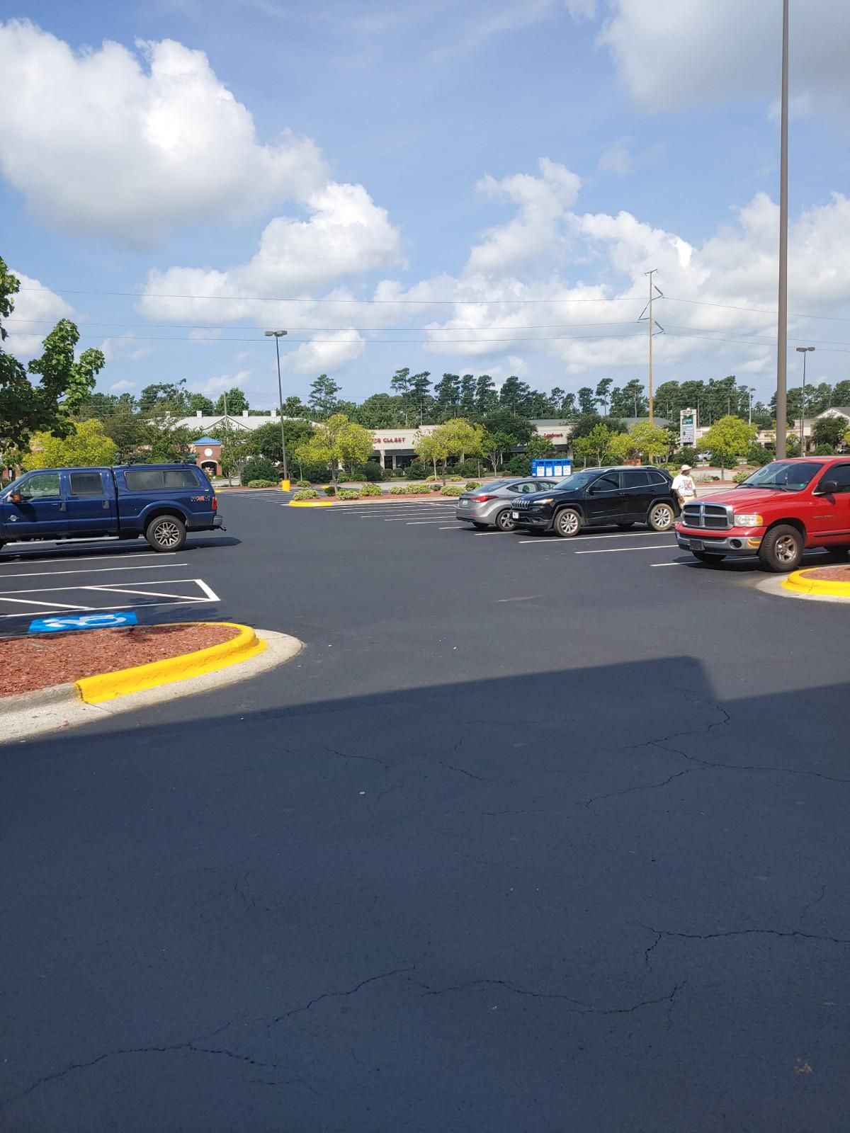 Parking lot with several cars parked. Blue sky and some clouds overhead.