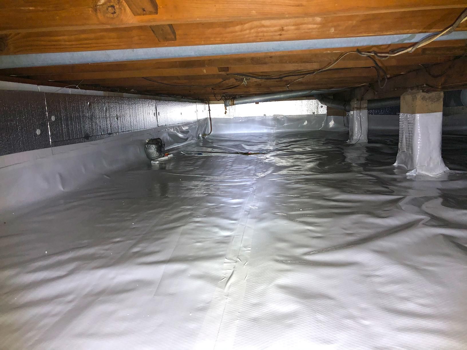 Crawl space with white vapor barrier covering the ground. Wood beams and supports are visible.