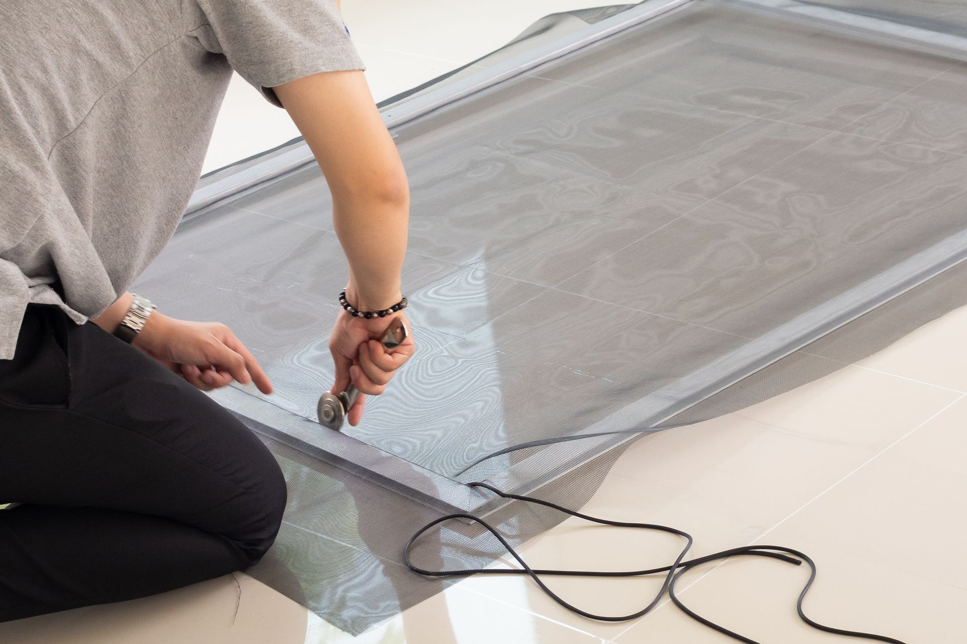 Person cutting screen mesh on a window frame, indoors.