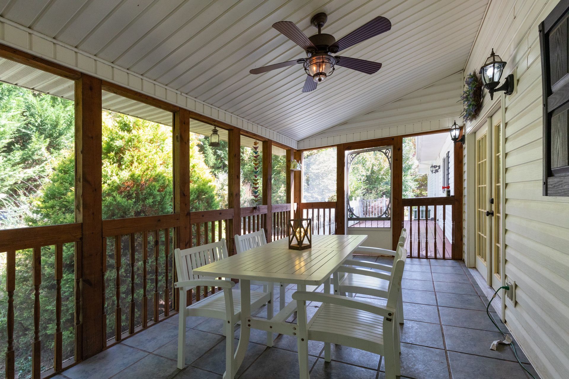 Screened porch with a white table and chairs, ceiling fan, and view of trees.