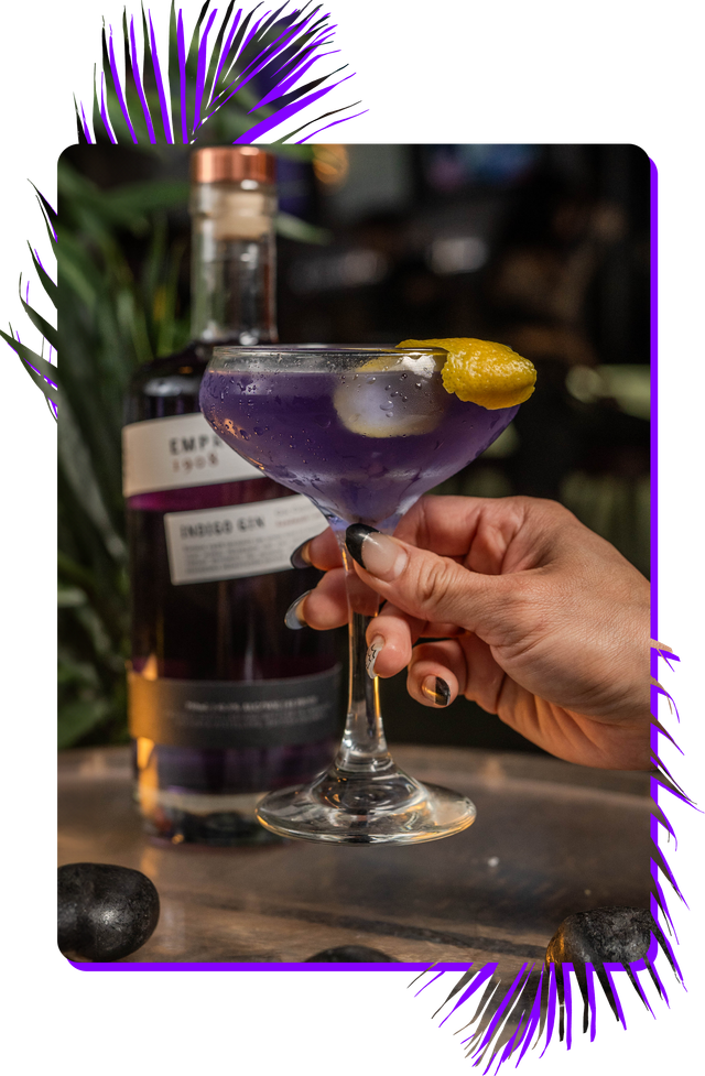 A woman is holding a purple martini in her hand.