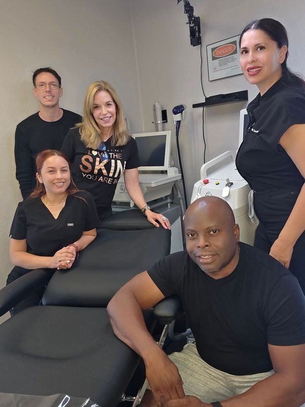 Group of five smiling people in a clinic setting. One man sits on a treatment bed.