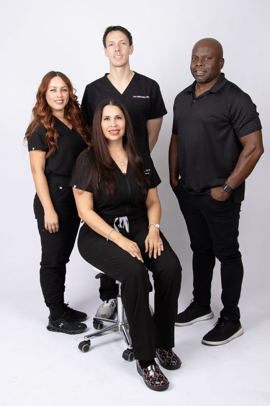 Four medical professionals in black scrubs pose for a group photo against a white background.