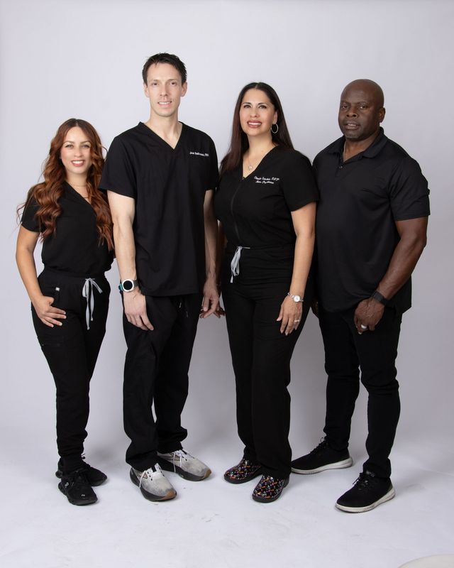 Four healthcare professionals in black scrubs pose against a gray background.