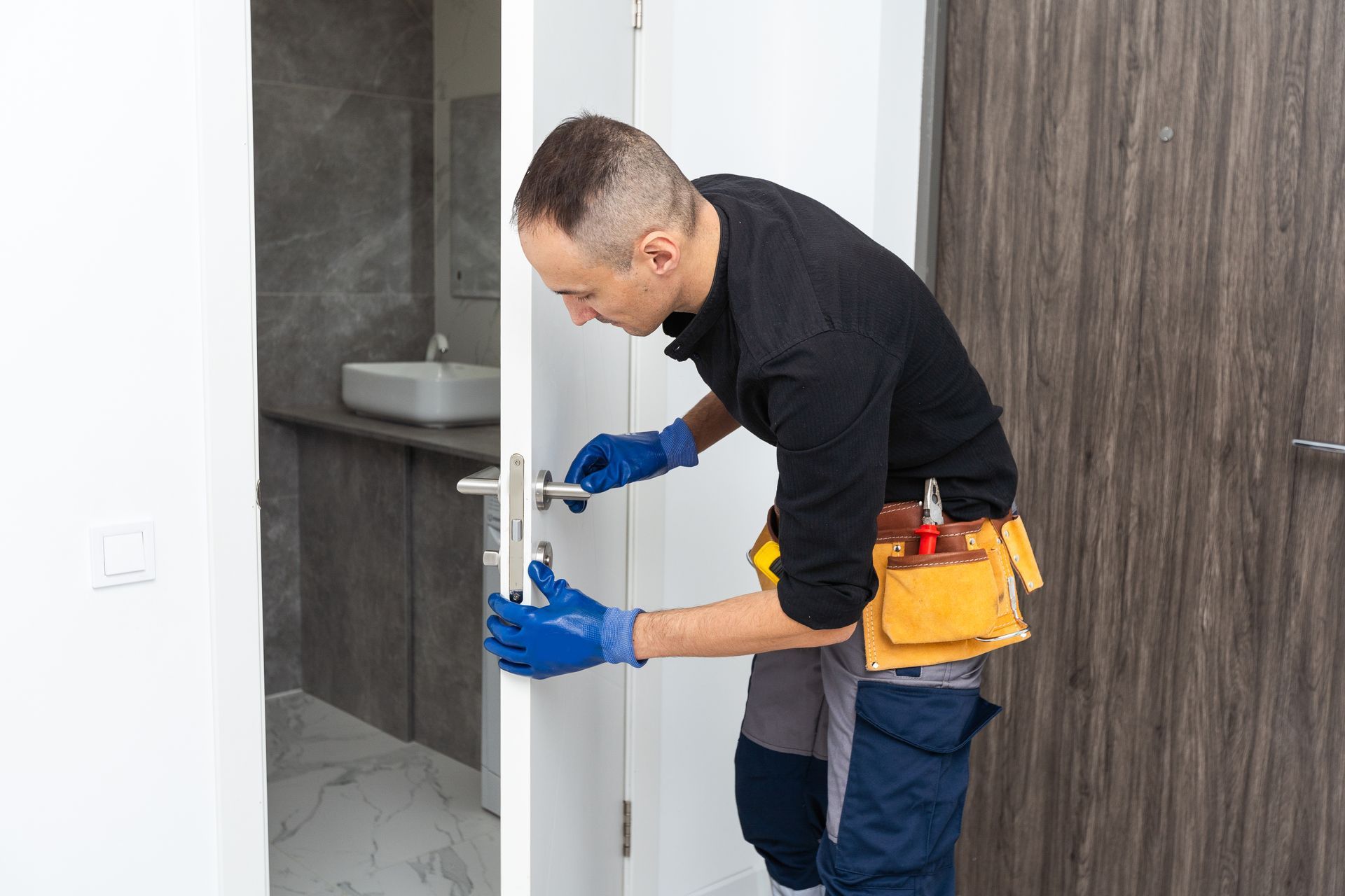 Technician in blue gloves installing a door handle in a bathroom doorway