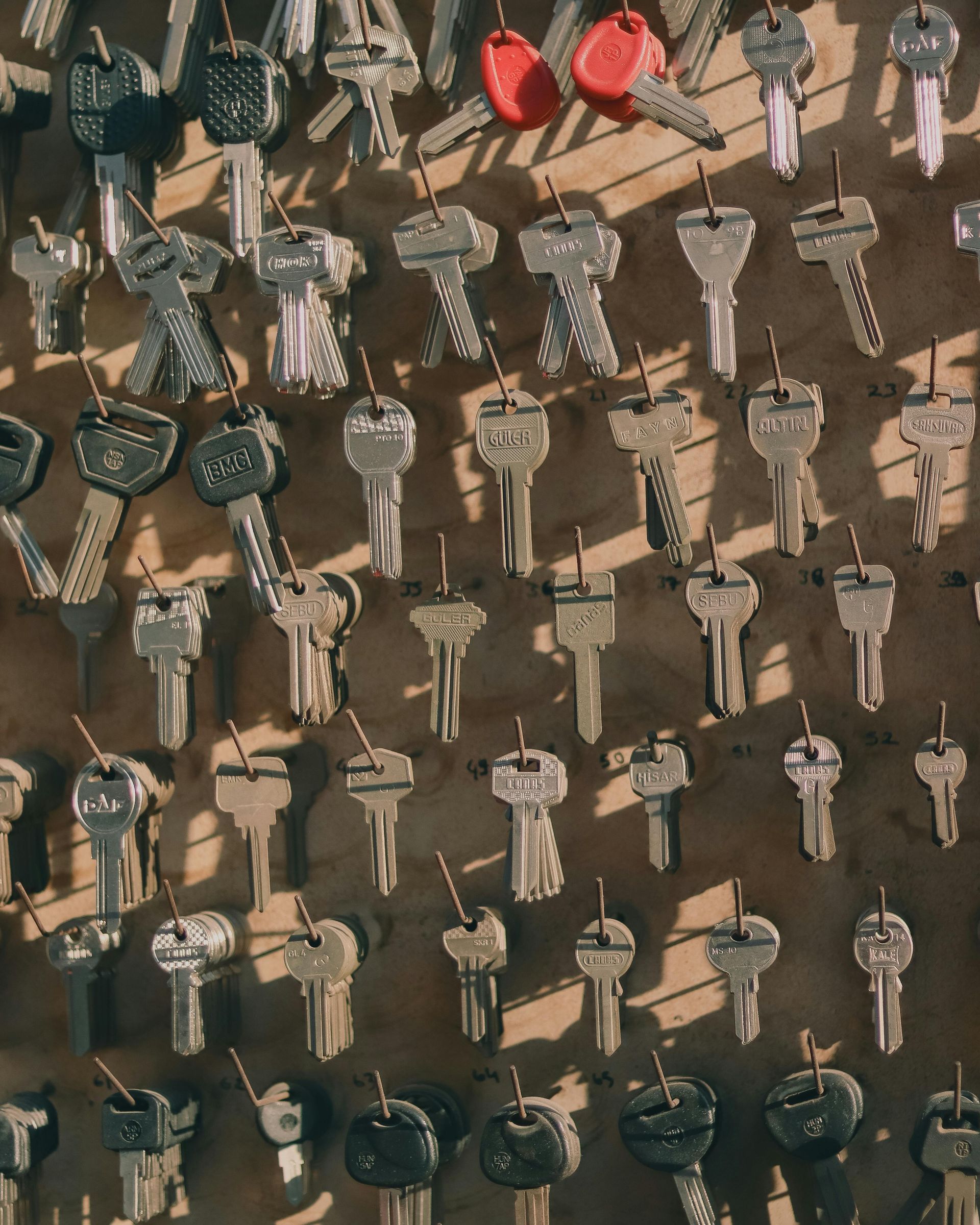 Dozens of assorted keys hanging on a wall display, mostly silver and black with a few red key covers.
