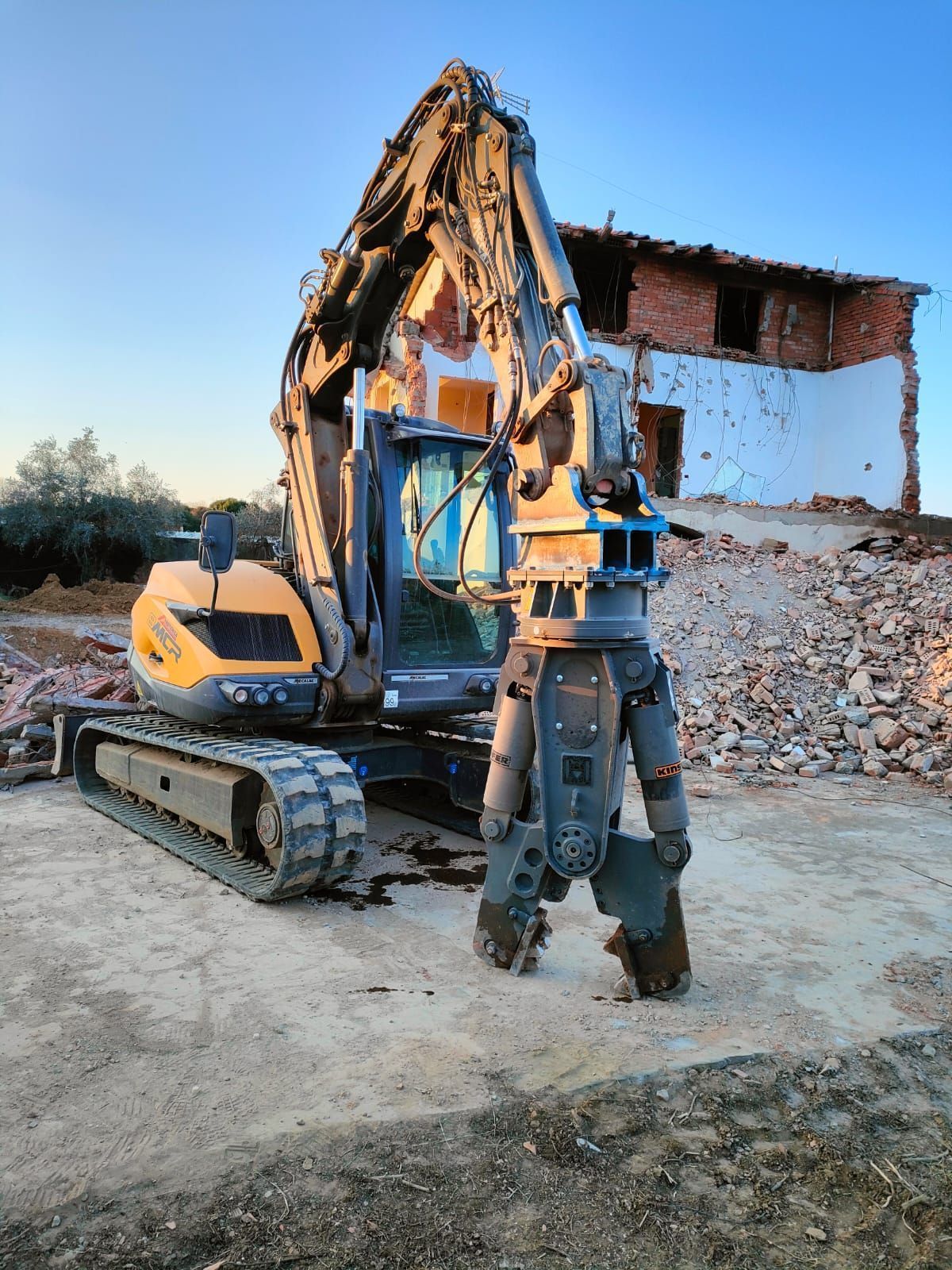Un grande escavatore è parcheggiato di fronte a un edificio in mattoni in fase di demolizione.