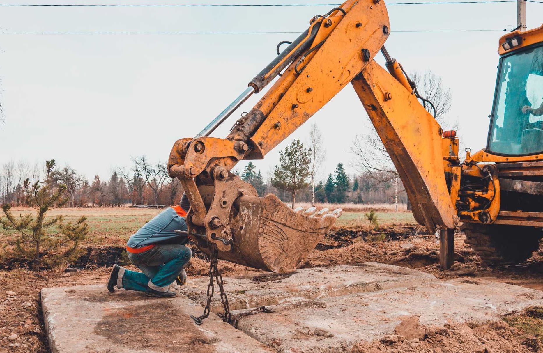 Un uomo è inginocchiato davanti a un escavatore giallo.