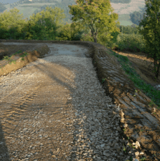 Una strada sterrata con un muro di pietra sul lato.