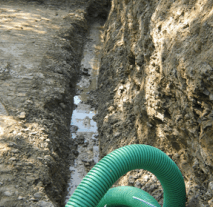 Un tubo verde è appoggiato nella terra accanto a un muro di roccia.