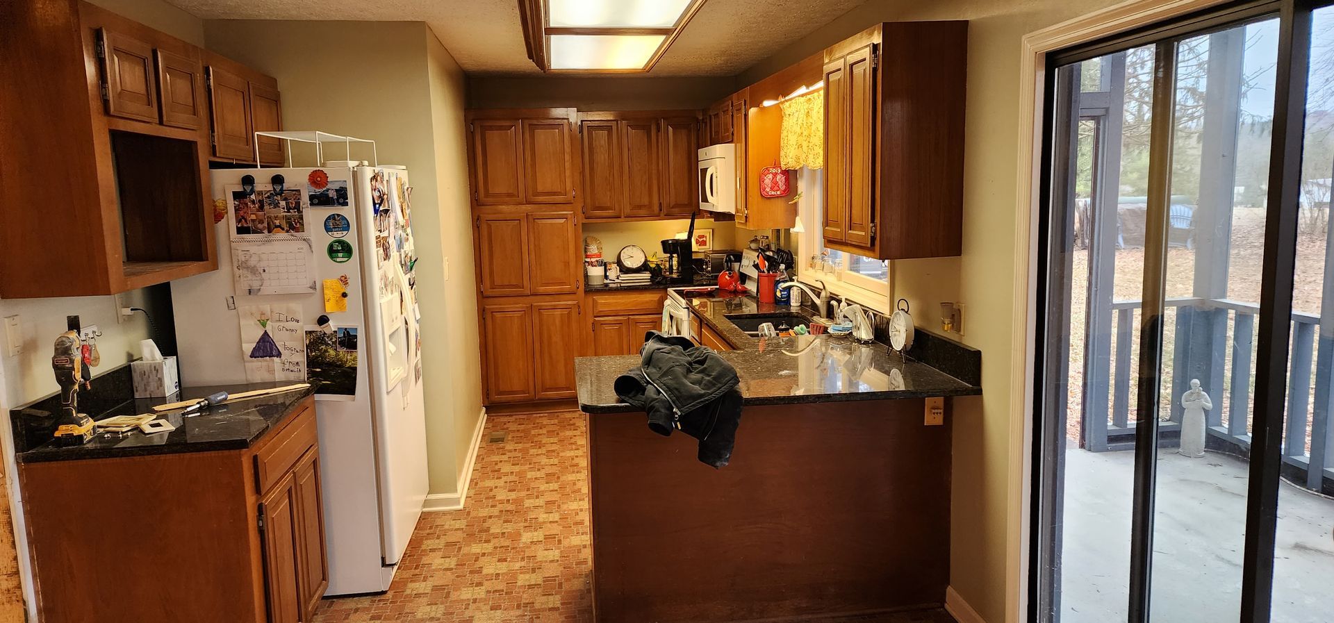 A kitchen with wooden cabinets , a refrigerator , a sink , and a sliding glass door.