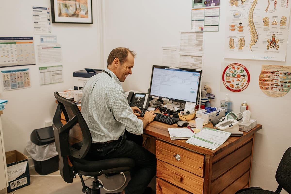 A Doctor Is Sitting at A Desk in Front of A Computer  — Rural Medical Clinic In Manilla, NSW