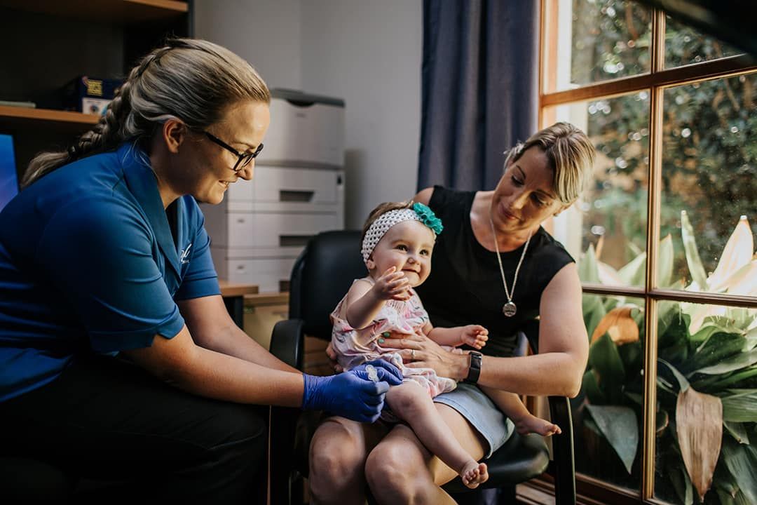 A Woman Is Holding a Baby in Her Lap — Rural Medical Clinic In Manilla, NSW