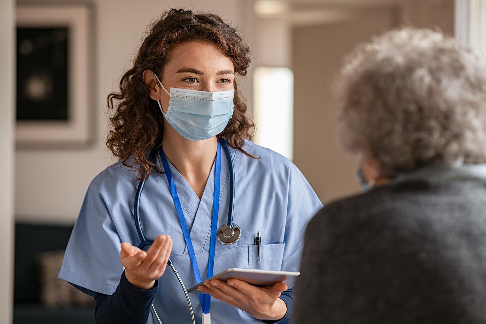 A Nurse Wearing A Mask Is Talking To An Elderly Woman — Rural Medical Clinic In Manilla, NSW