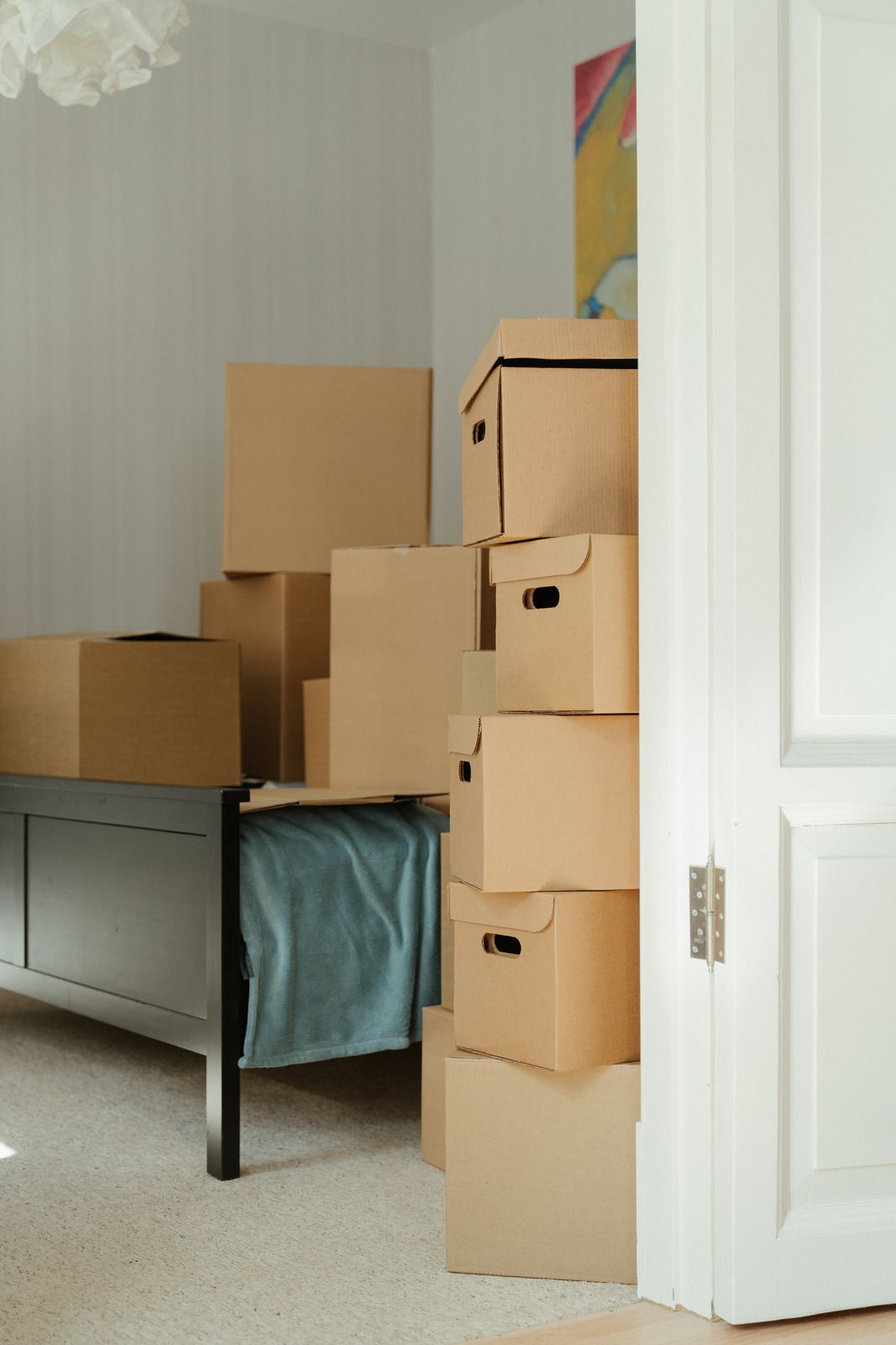 Stacked cardboard boxes in a doorway beside a bed in a sparse room